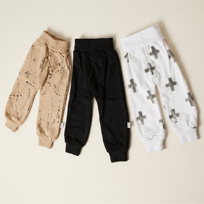 Three pairs of baby leggings in beige, black, and white with patterns on a beige background.