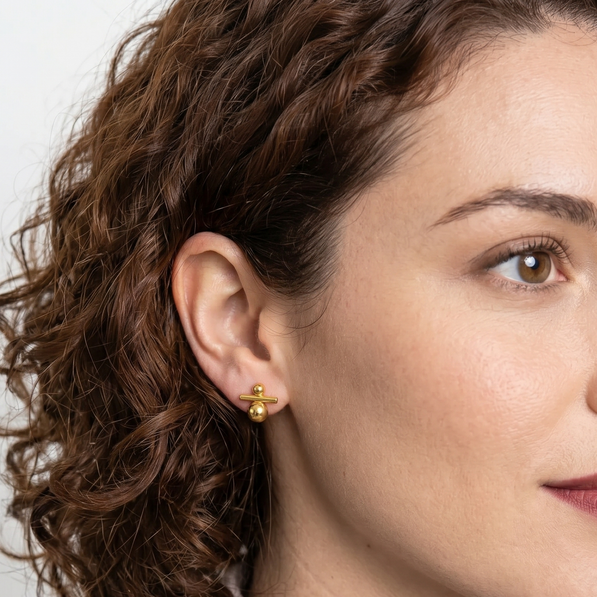 Woman wearing gold earrings with a neutral background