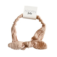 Beige headband with a bow on a striped fabric background, featuring 'ADORN kids' branding.
