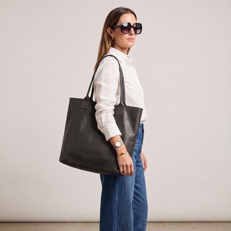 Woman holding a black leather tote bag against a plain background