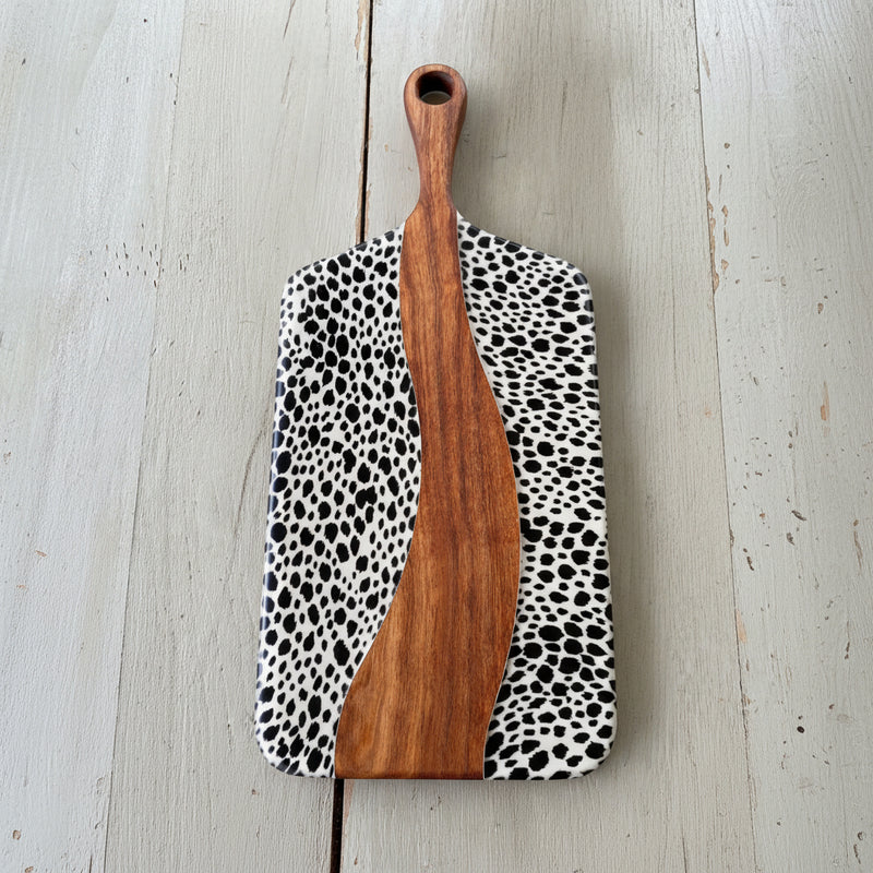 Wooden paddle cheeseboard with a black and white pattern on a light wooden surface