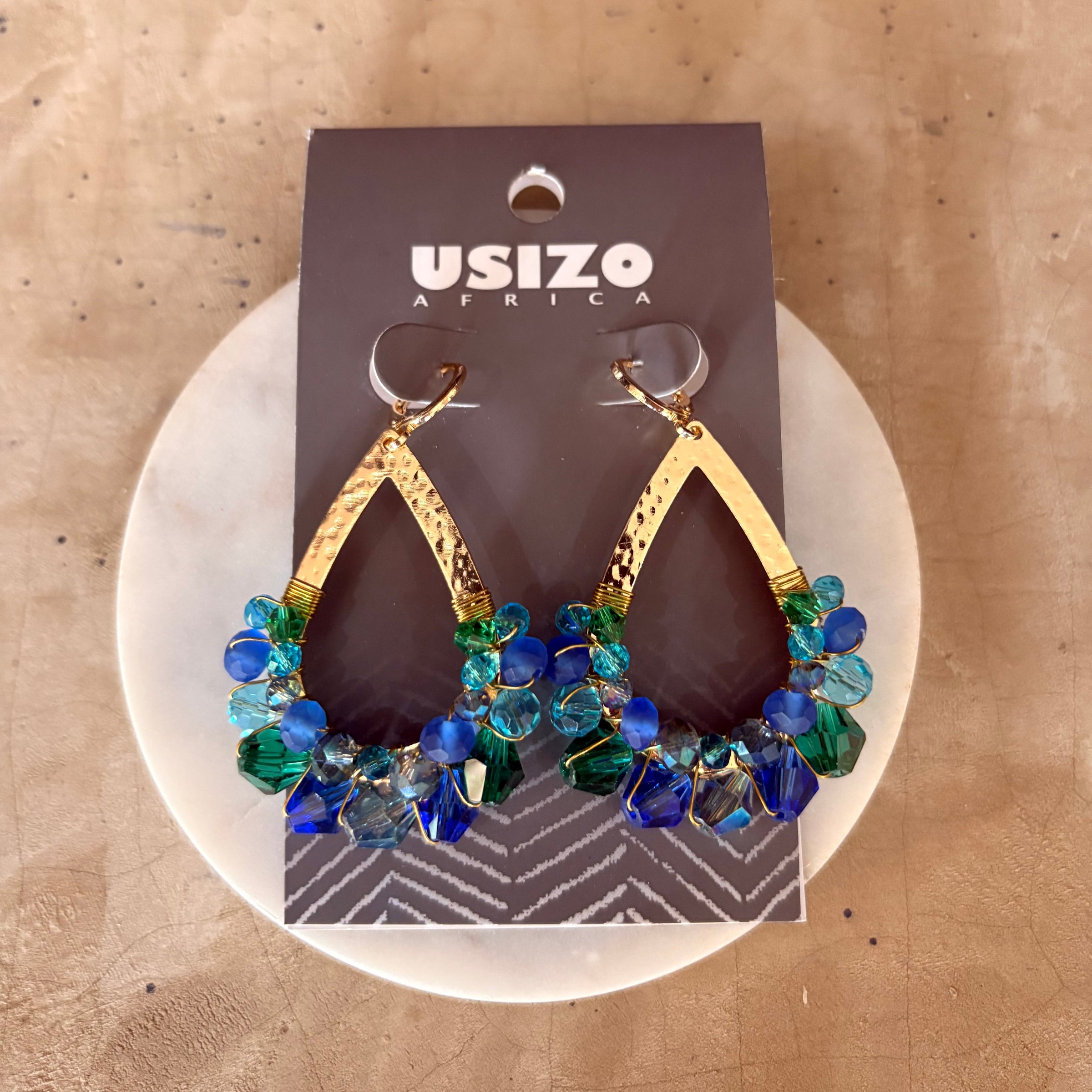 Gold and blue beaded earrings on a Usizo branded card against a beige background