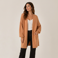 Woman wearing a clay cardigan over a white top and pants on a beige background
