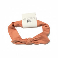 Peach-colored headband with 'Adorn Kids' packaging on a gray surface