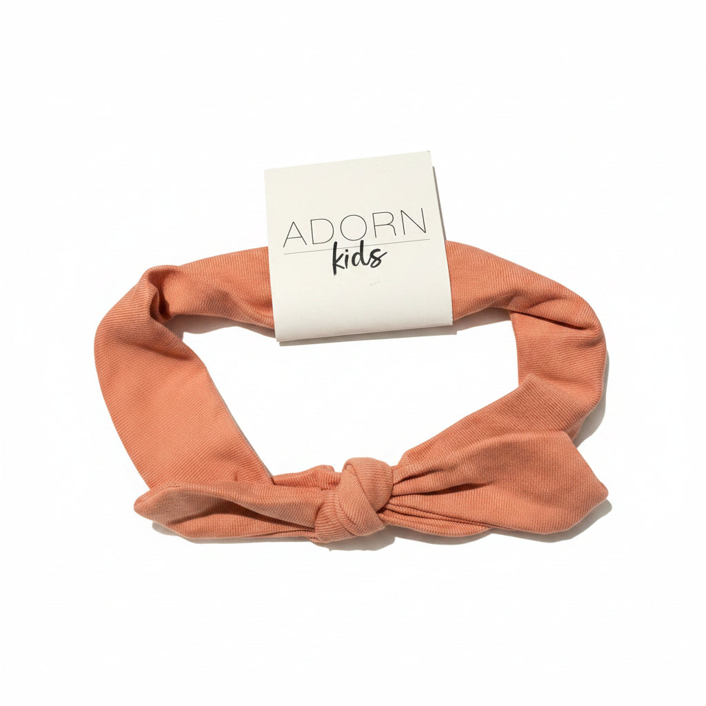 Peach-colored headband with 'Adorn Kids' packaging on a gray surface