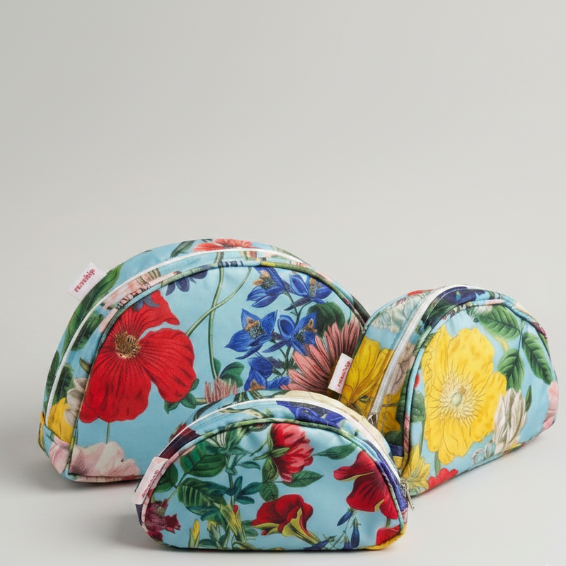 Three floral zippered cosmetic pouches in different sizes arranged on a light gray background. The pouches feature a light blue base with a vibrant botanical print including red poppies, yellow flowers, pink blossoms, and green leaves.