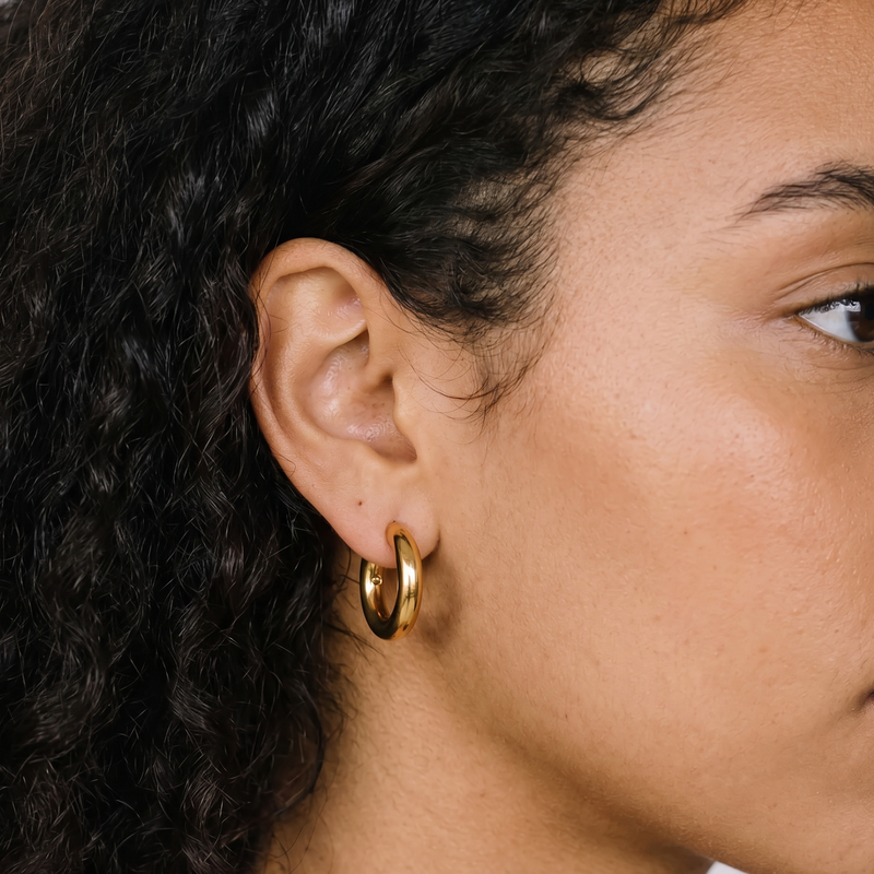 Close-up of a person wearing a gold hoop earring with a neutral background