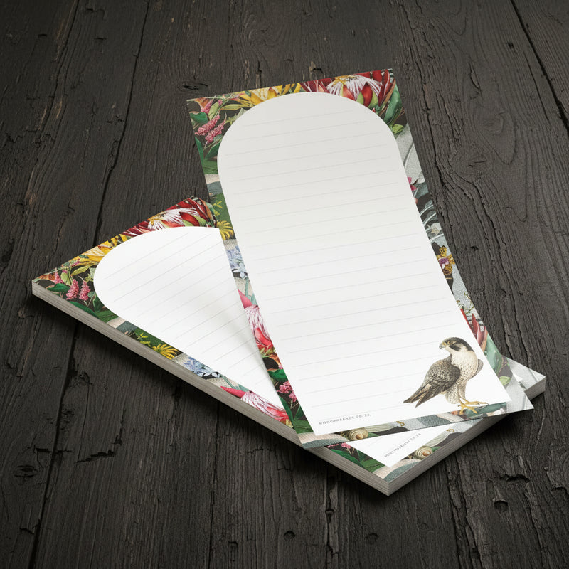 A stack of lined notepads with a tropical floral border and a bird illustration on the cover, placed on a light wood surface.