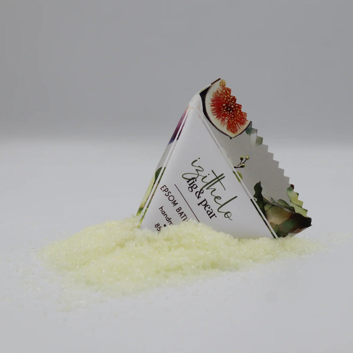 A triangular foil packet labeled 'bytholo Dark Pear' stands partly embedded in a small pile of pale yellow crystalline powder on a light gray studio background.