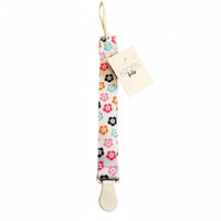 Floral-patterned pacifier clip with a 'Adorn Kids' tag on a brown surface