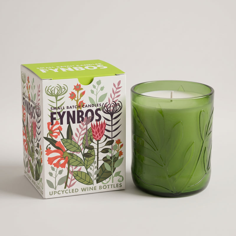 A green glass candle jar next to its illustrated product box. The box reads 'SONYBOS' and 'SMALL BATCH CANDLES' with 'UPCYCLED WINE BOTTLES' at the bottom, featuring botanical line drawings in pink, red, green, and black on a white background.