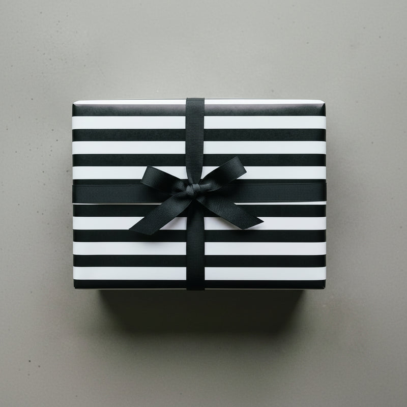 Black and white striped gift box with a bow on a wooden surface, next to a coffee cup and succulent plant.