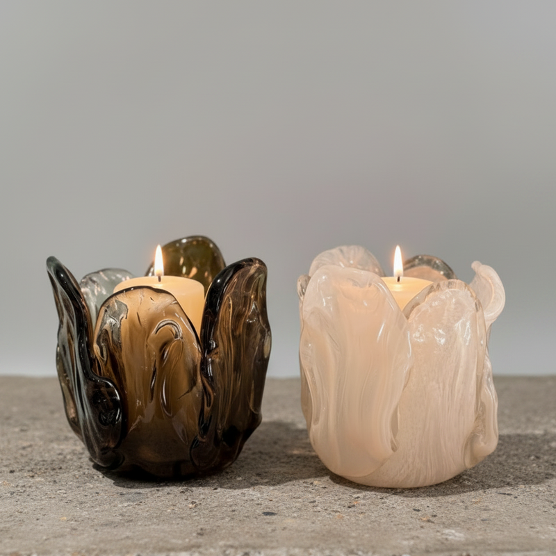 Two glass candle holders with lit candles on a wooden surface.