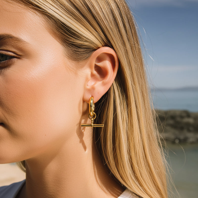 Close-up of a gold earring worn by a person with a blurred natural background