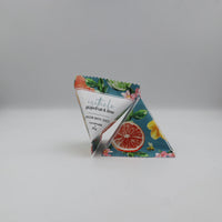 Two triangular bath salts packets with a colorful citrus and floral design, standing upright on a light gray background. The front packet shows the brand name 'isothelo' and the scent 'grapefruit & lime'.