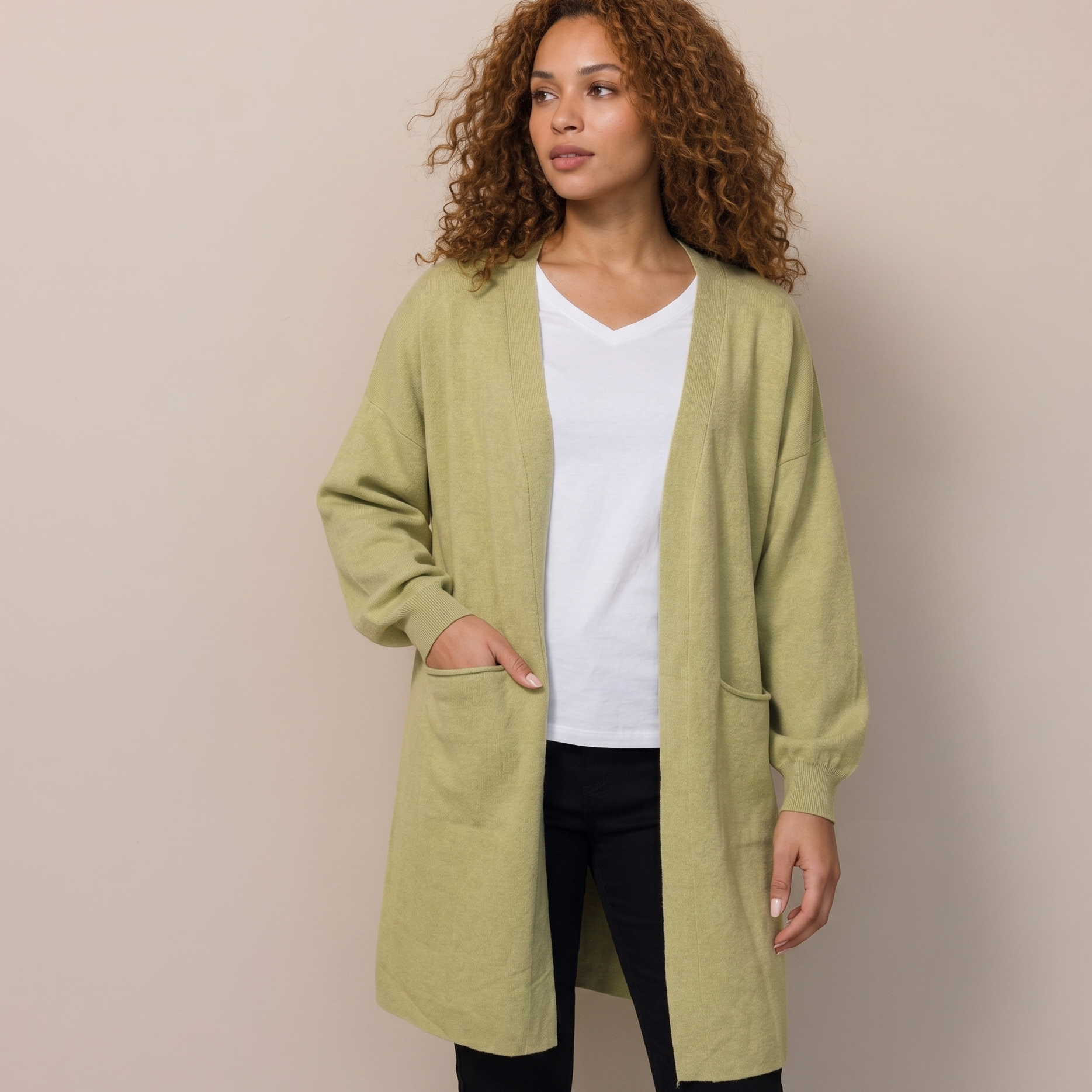 Woman wearing a green cardigan over a white shirt and black pants on a beige background
