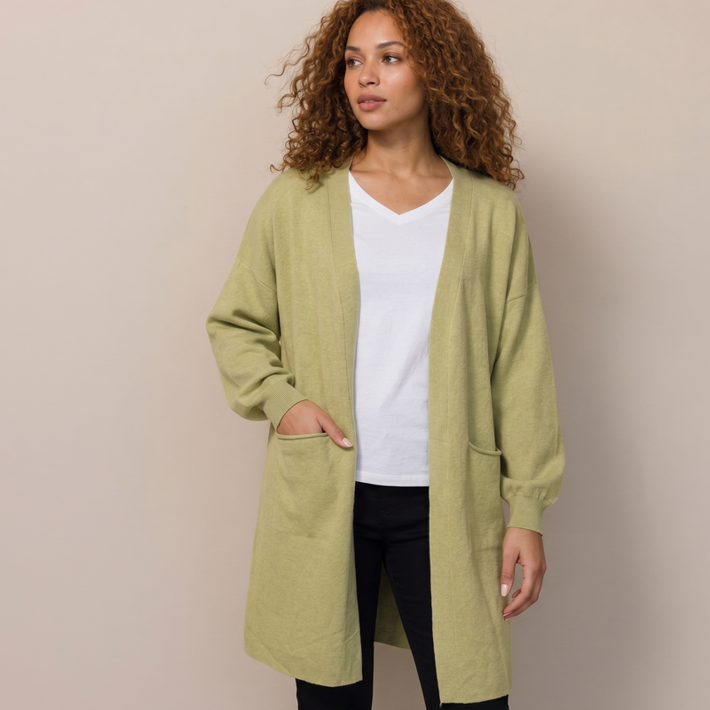 Woman wearing a green cardigan over a white shirt and black pants on a beige background