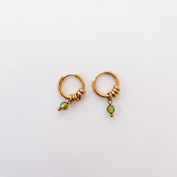 A pair of gold huggie hoop earrings with textured wrap details and a small green faceted bead dangle, shown on a plain white background.