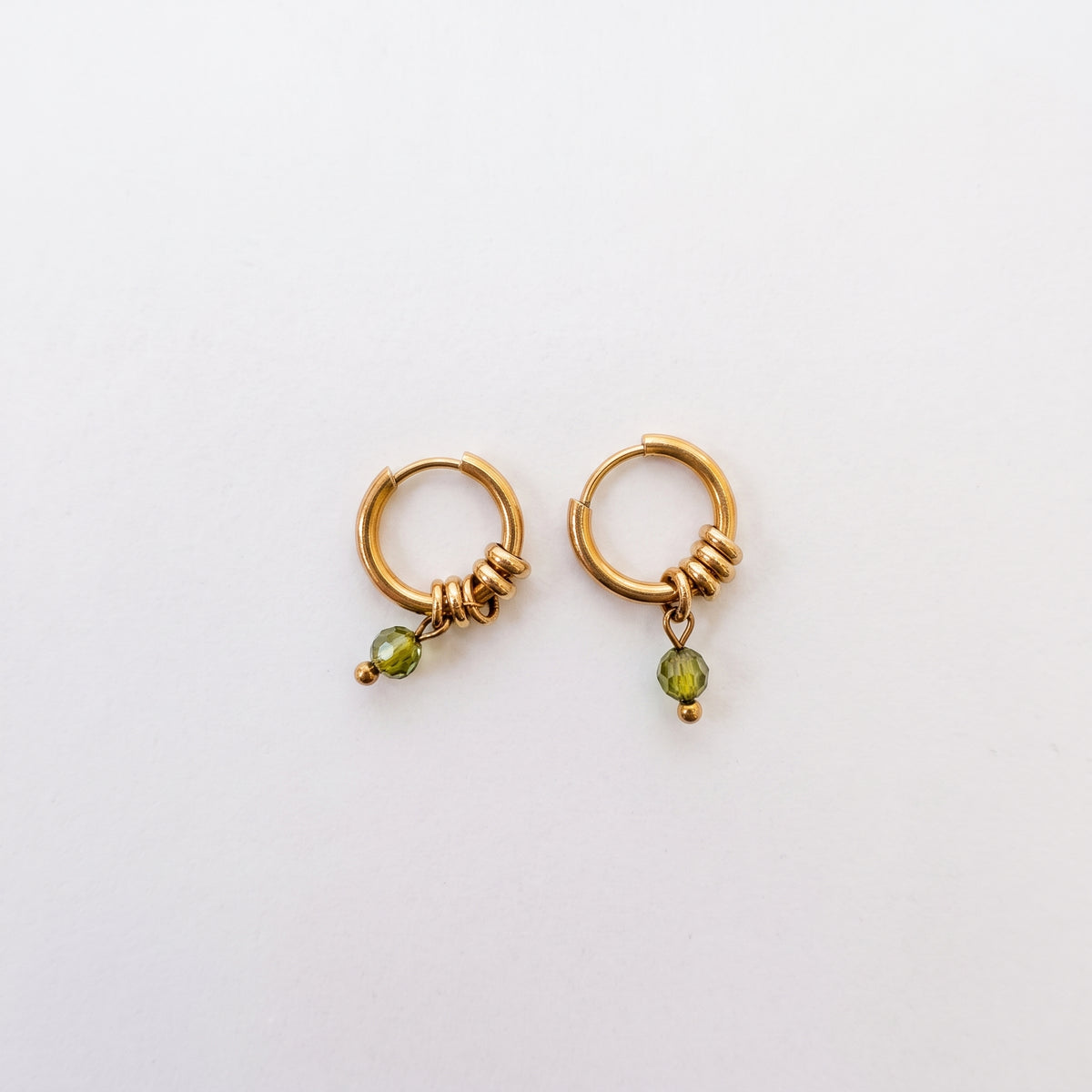 A pair of gold huggie hoop earrings with textured wrap details and a small green faceted bead dangle, shown on a plain white background.