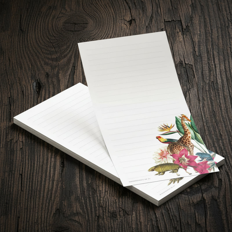 A stack of lined notepads on a light wood tabletop, with the top pad partially open to show a colorful tropical bird and floral illustration in the lower right corner.