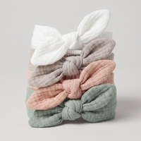 Set of four fabric hair bows in white, gray, pink, and green on a light gray background