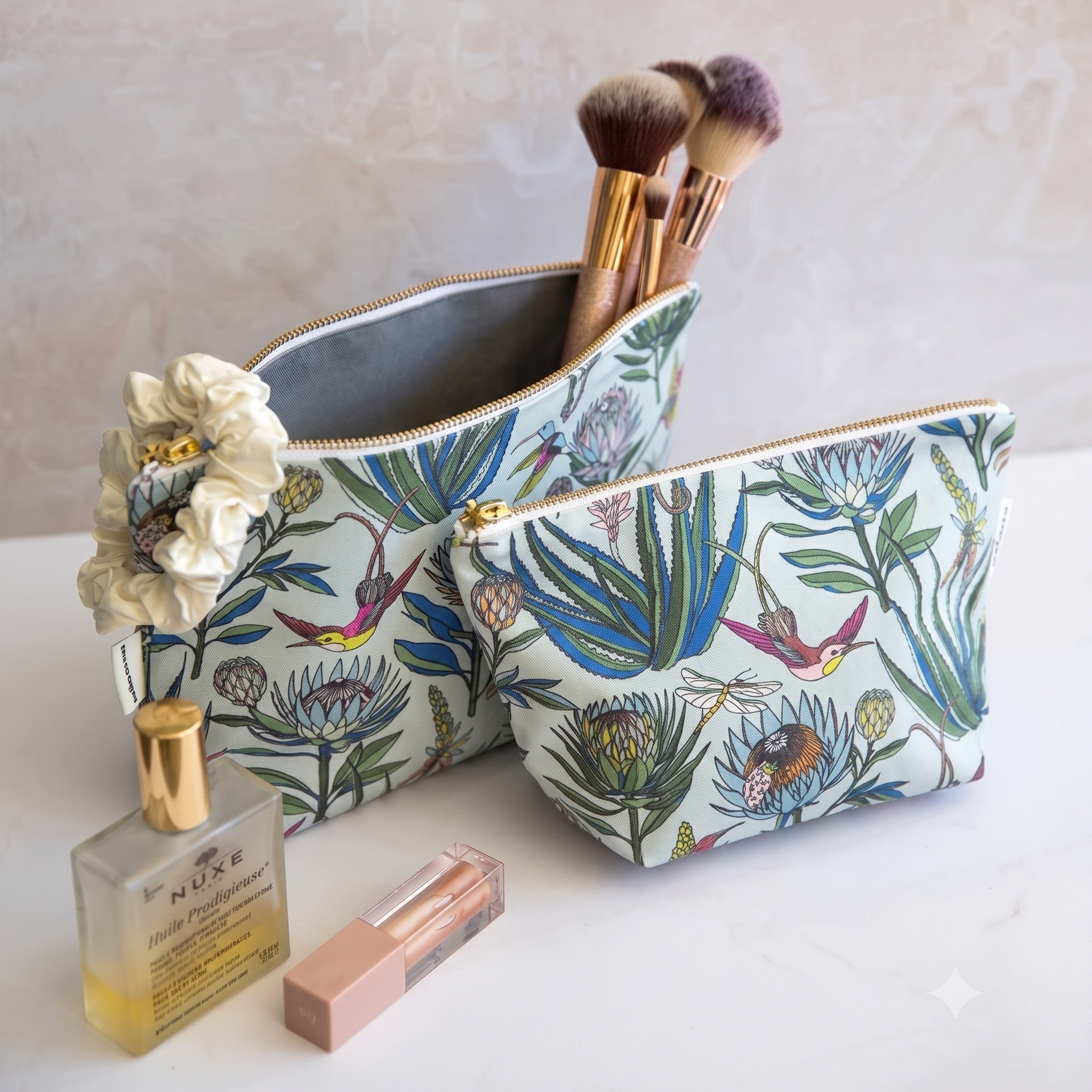 Floral-patterned makeup bag with brushes, a perfume bottle, and lip balm on a light surface.