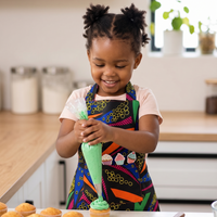 Child in a kitchen wearing a colorful apron, decorating cupcakes with frosting.