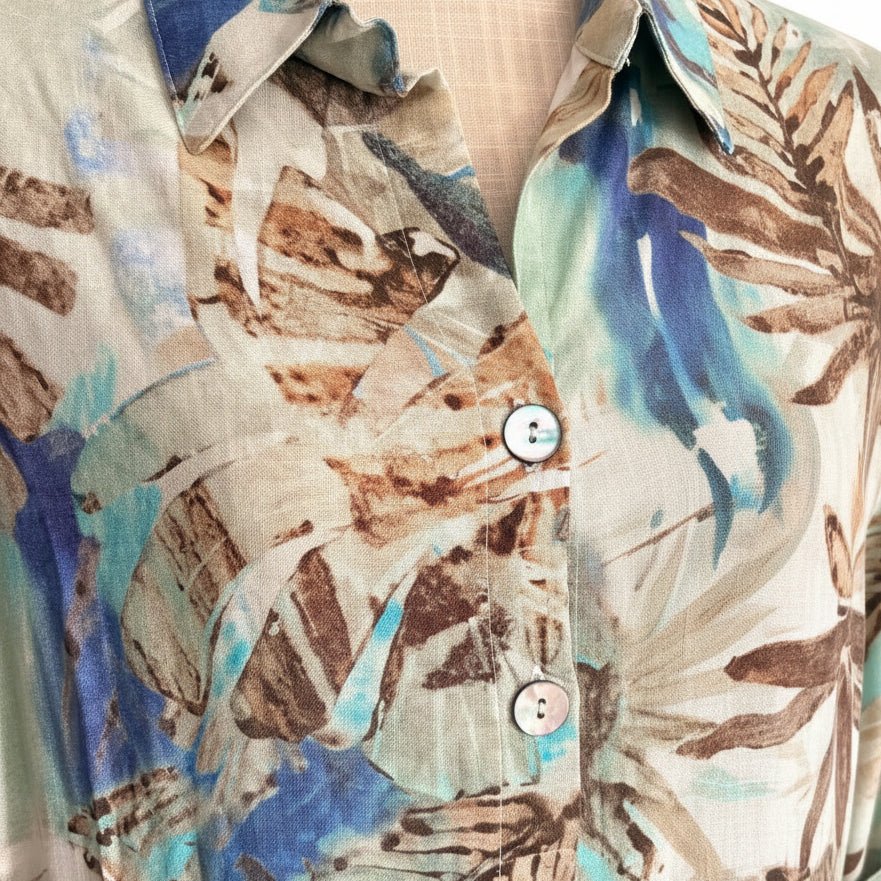 A close-up of a button-front shirt with an abstract botanical print in beige, brown, blue, and turquoise tones.