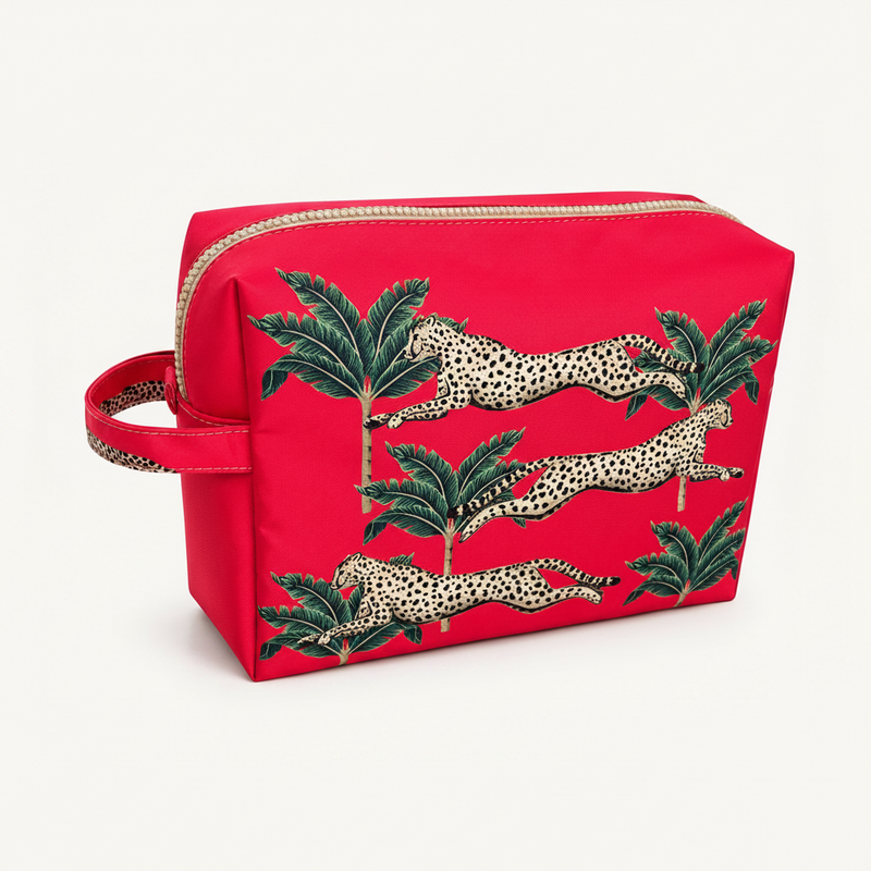 A bright cerise zippered cosmetic pouch featuring an embroidered design of leaping cheetahs and green palm trees, shown on a clean white background.