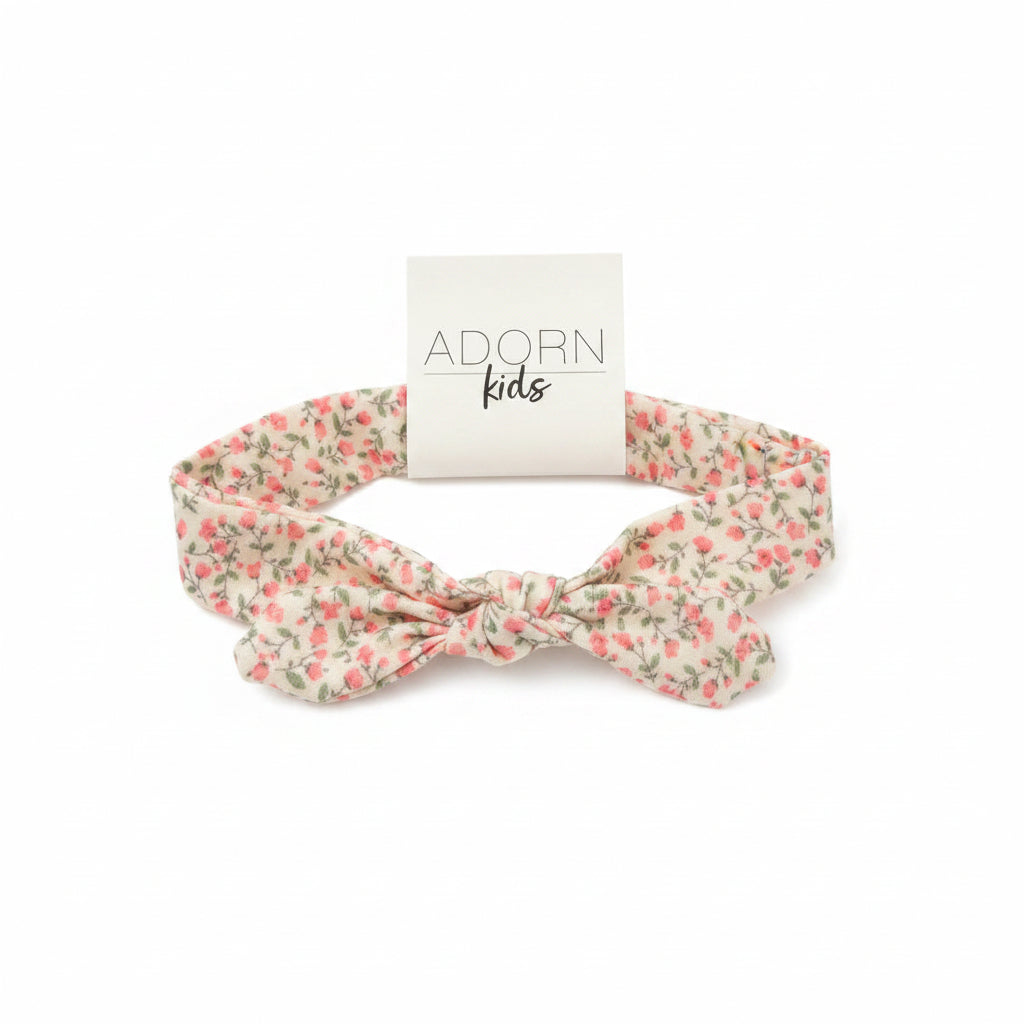 Floral headband with 'Adorn Kids' tag on a wooden surface