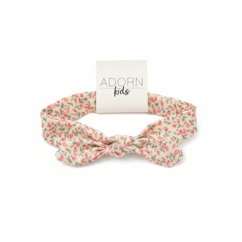 Floral headband with 'Adorn Kids' tag on a wooden surface