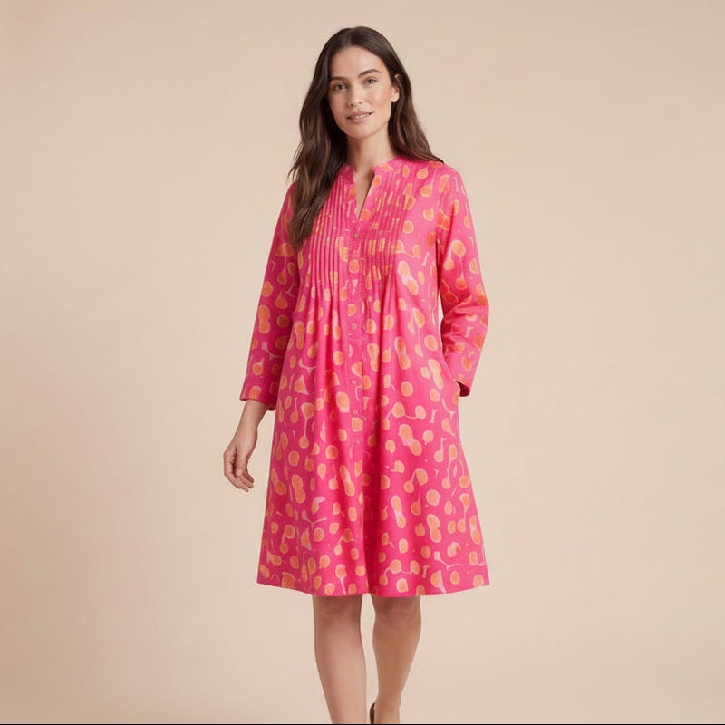 A woman modeling a pink smocked long-sleeve dress with a yellow and orange paisley pattern, standing against a solid beige studio background.