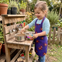 Child playing with pots and pans on a wooden play kitchen set outdoors.