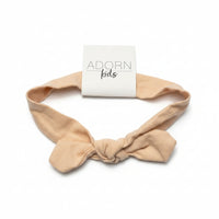 Beige headband with a 'ADORN kids' sign on a gray surface