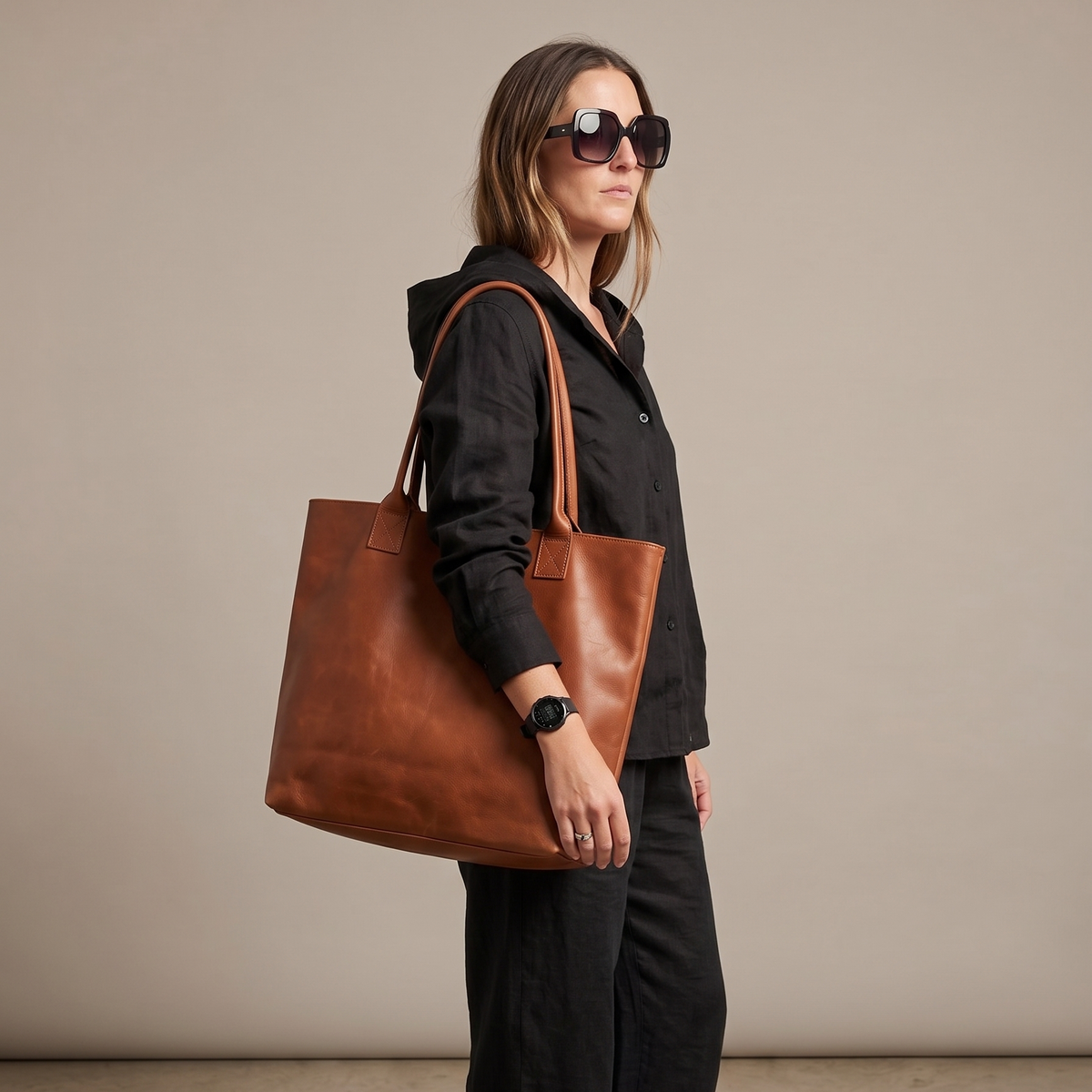 Woman holding a brown leather tote bag against a neutral background