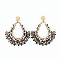 Pair of ornate earrings on a branded card against a textured beige background
