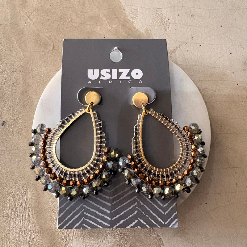 Pair of ornate earrings on a branded card against a textured beige background