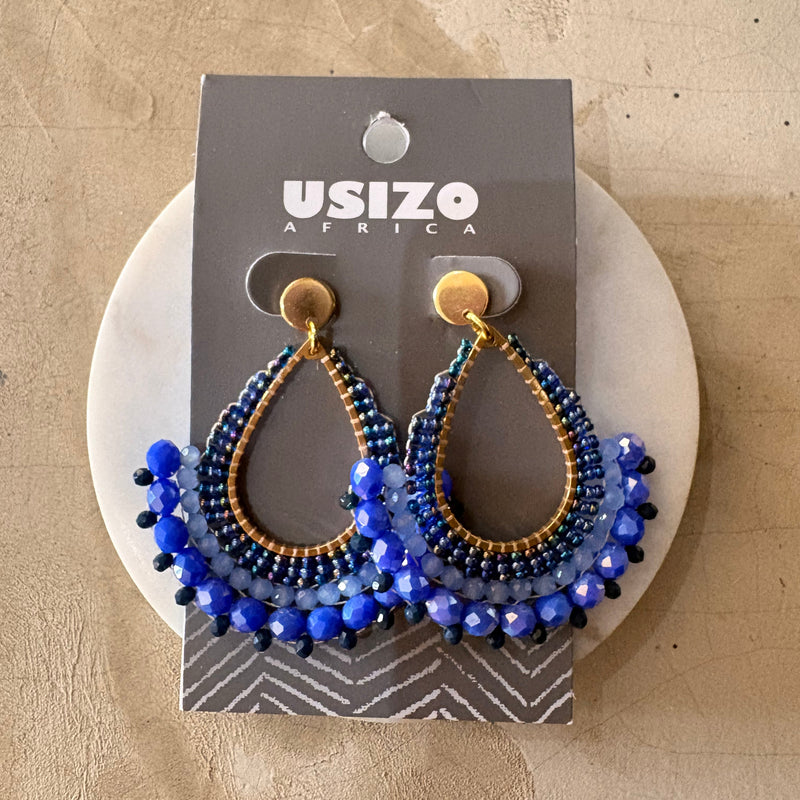 Blue beaded earrings on a Usizo branded card against a beige background
