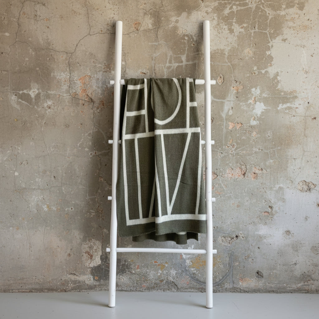 Brown blanket with white geometric pattern draped over a ladder against a light green wall.