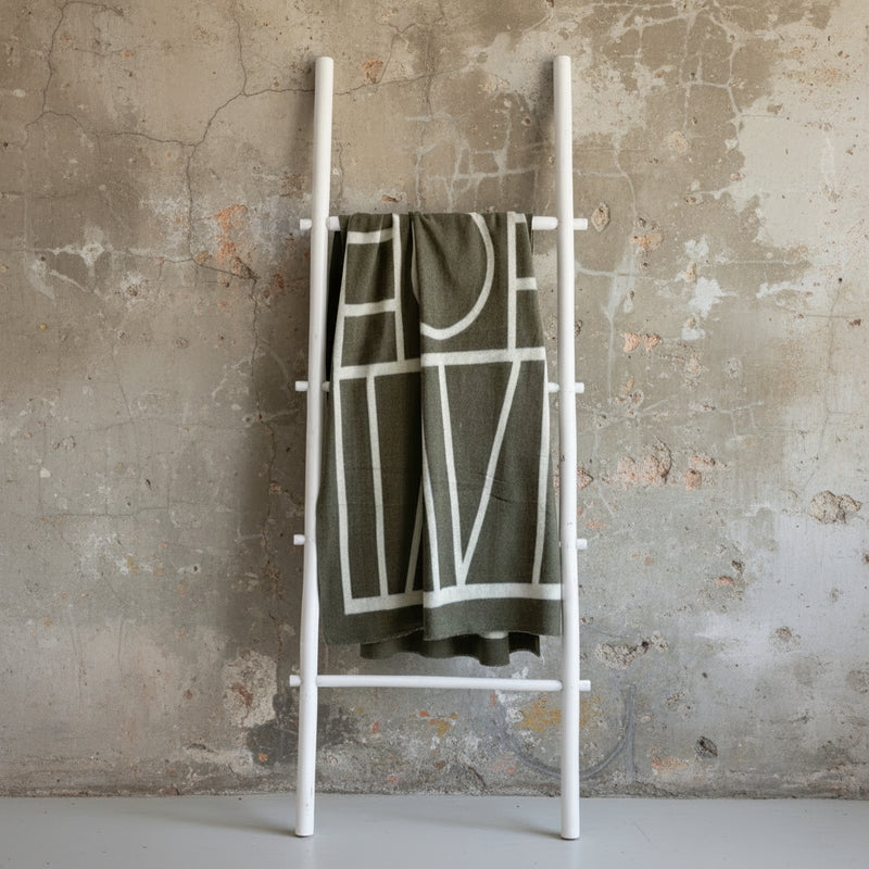 Brown blanket with white geometric pattern draped over a ladder against a light green wall.