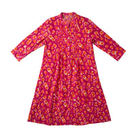 A pink long-sleeve tunic dress with an orange and yellow abstract pattern, laid flat on a light gray fabric background.