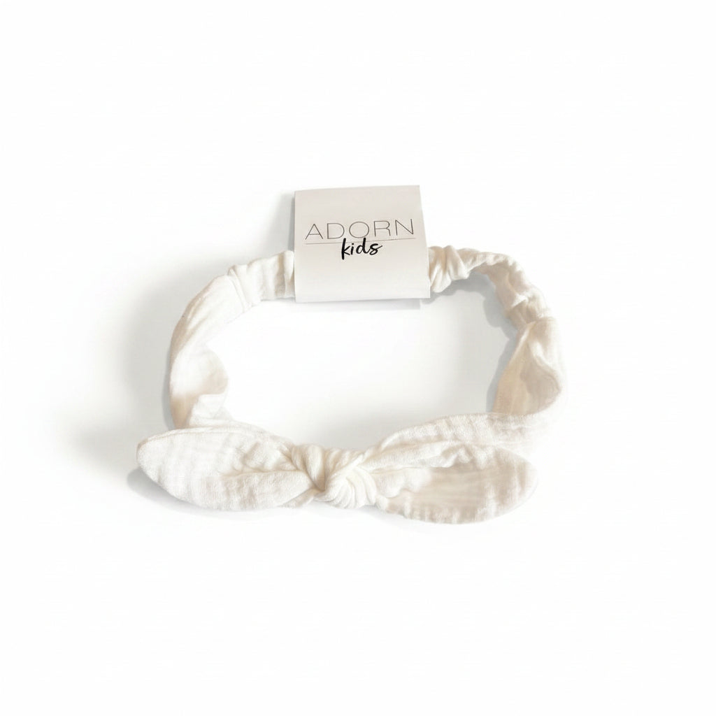 White headband with bow on a striped fabric background, featuring 'Adorn Kids' branding.