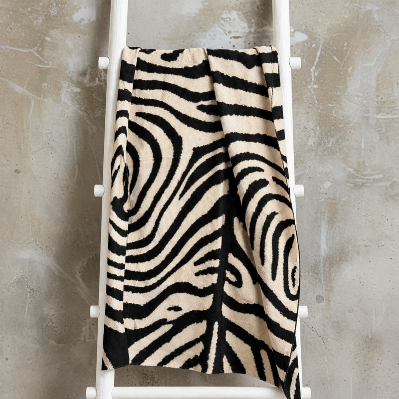Zebra patterned blanket draped over a white ladder against a beige wall.